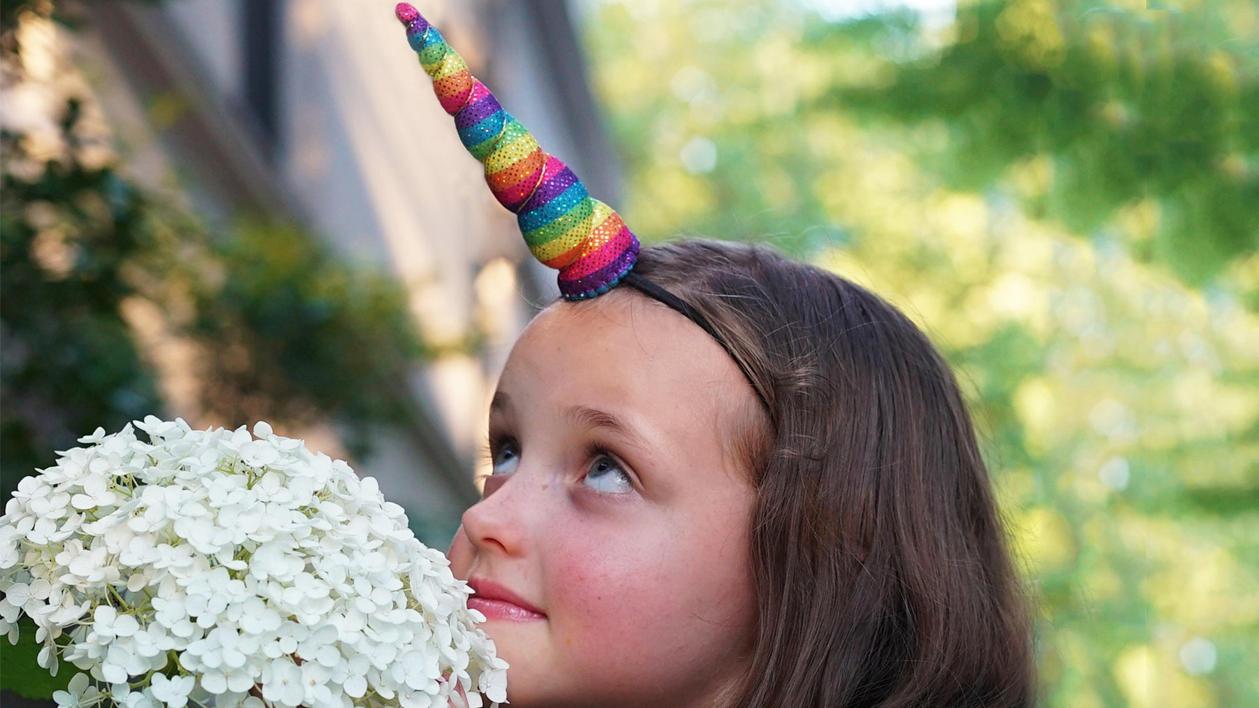 Little girl wearing unicorn horn near hydrangea flowers